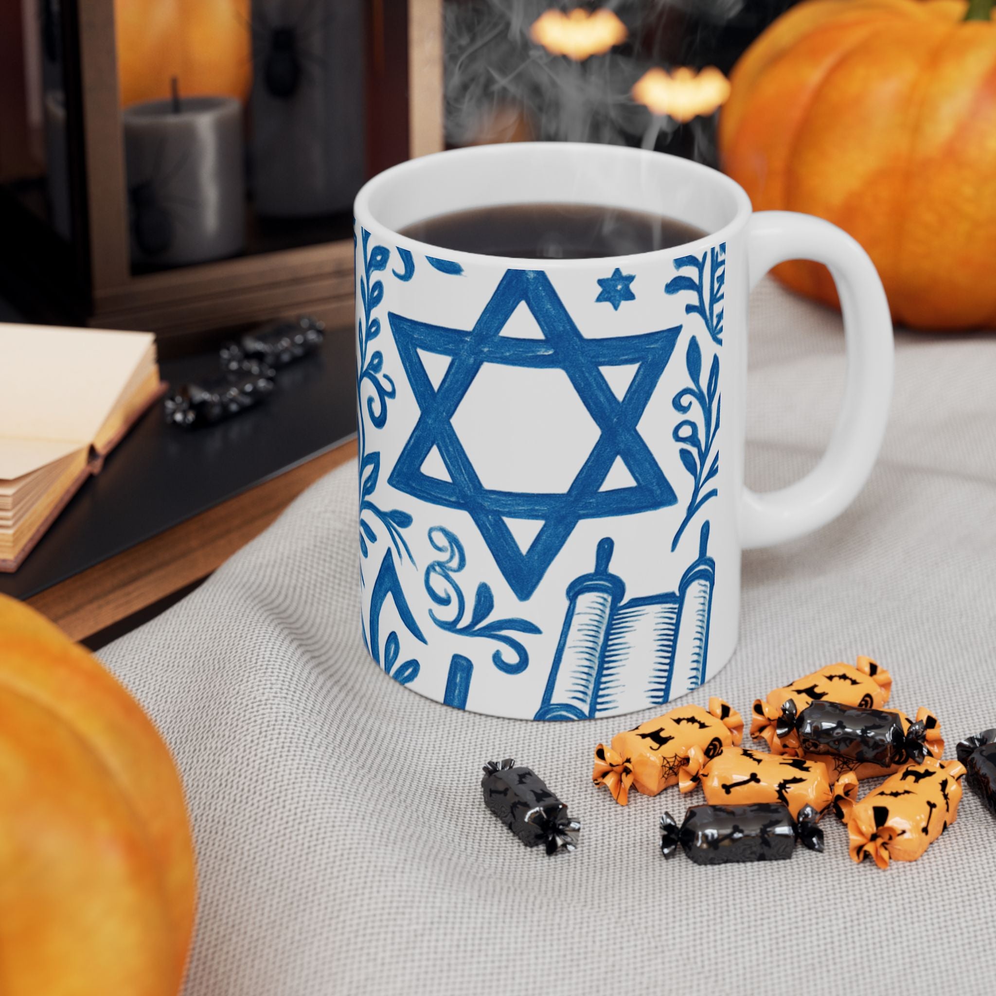 Mug with Star of David design on a table with Halloween-themed treats and pumpkins.