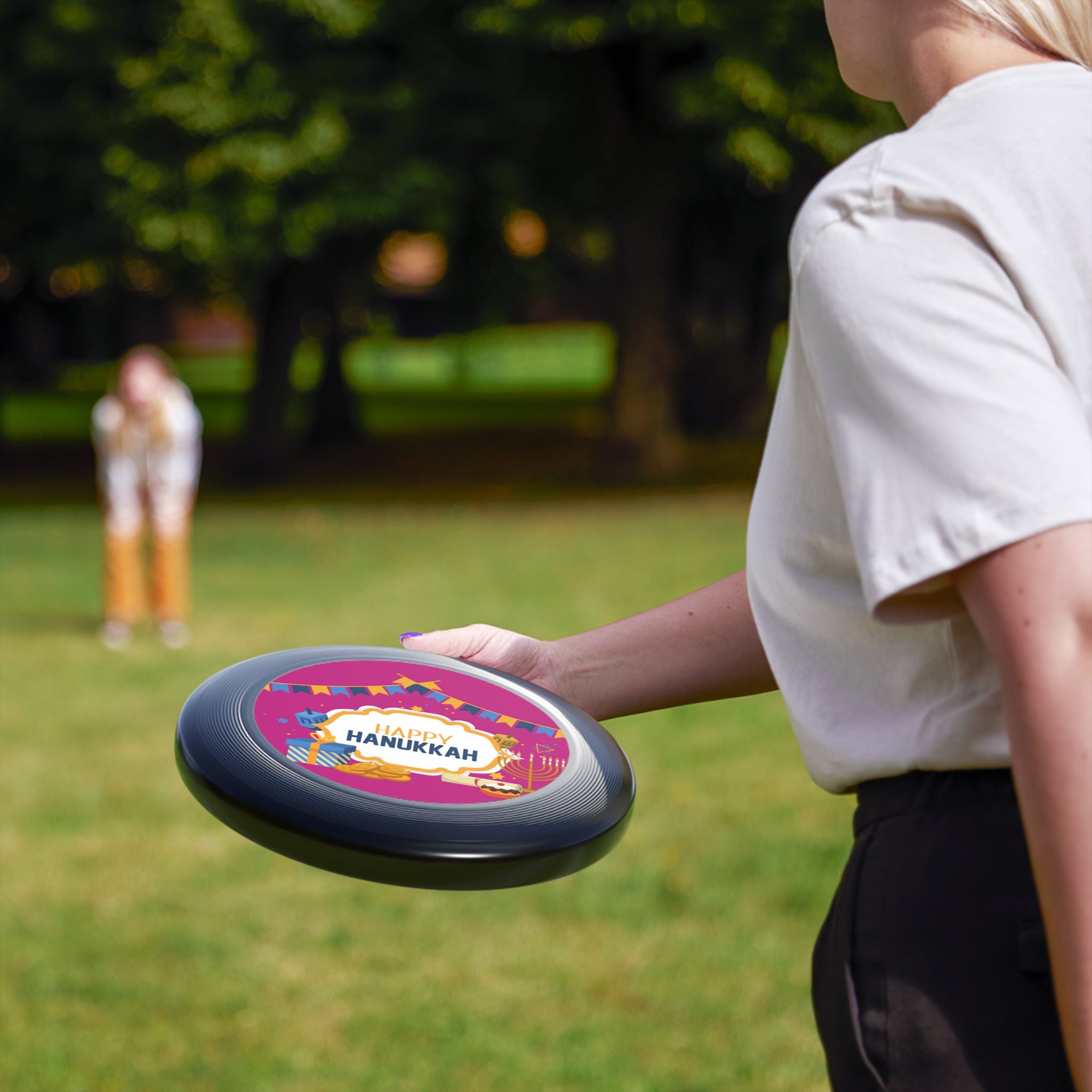 Person holding a colorful frisbee with 'Happy Hanukkah' text in a park setting