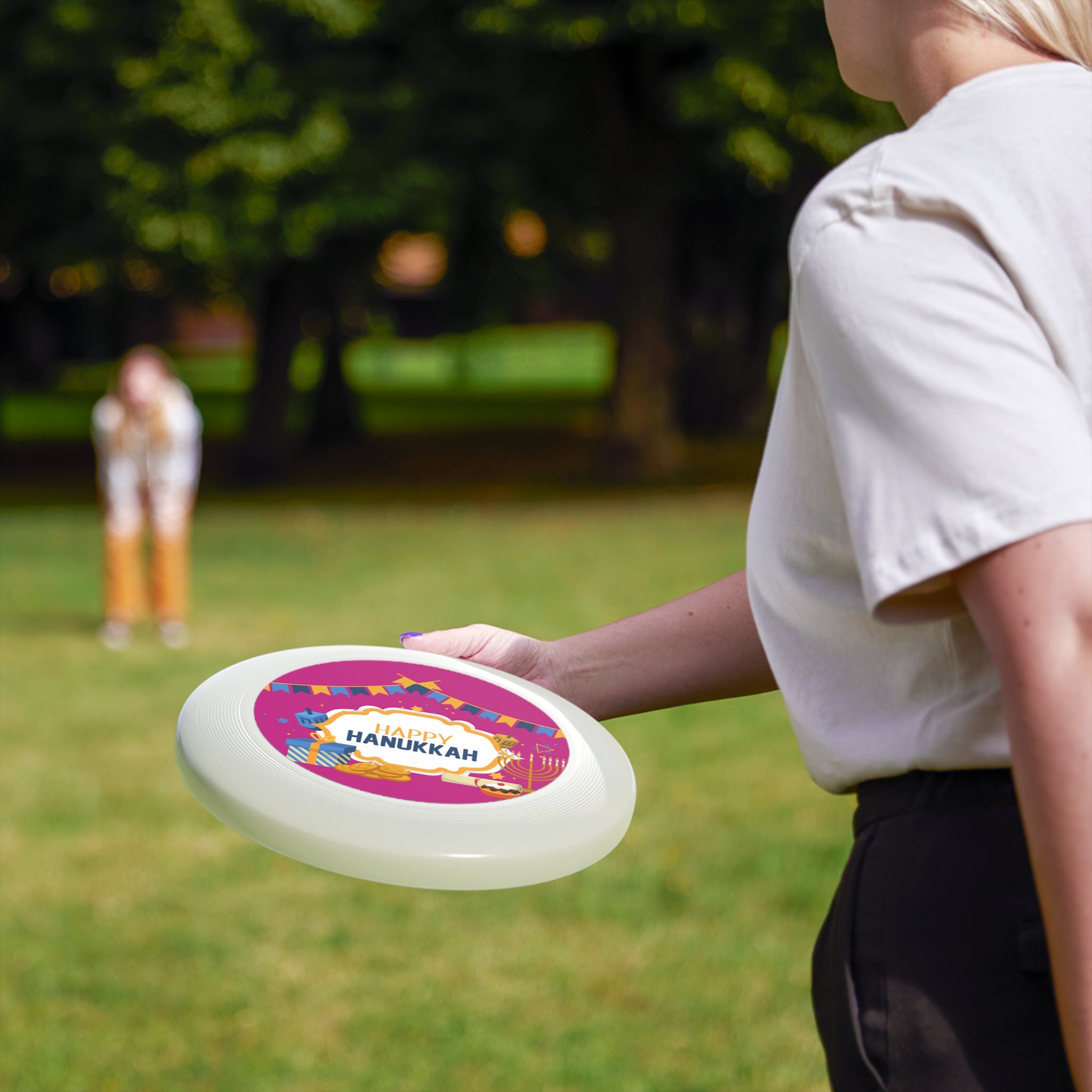 Person holding a colorful frisbee with 'Hanukkah' text in a park setting