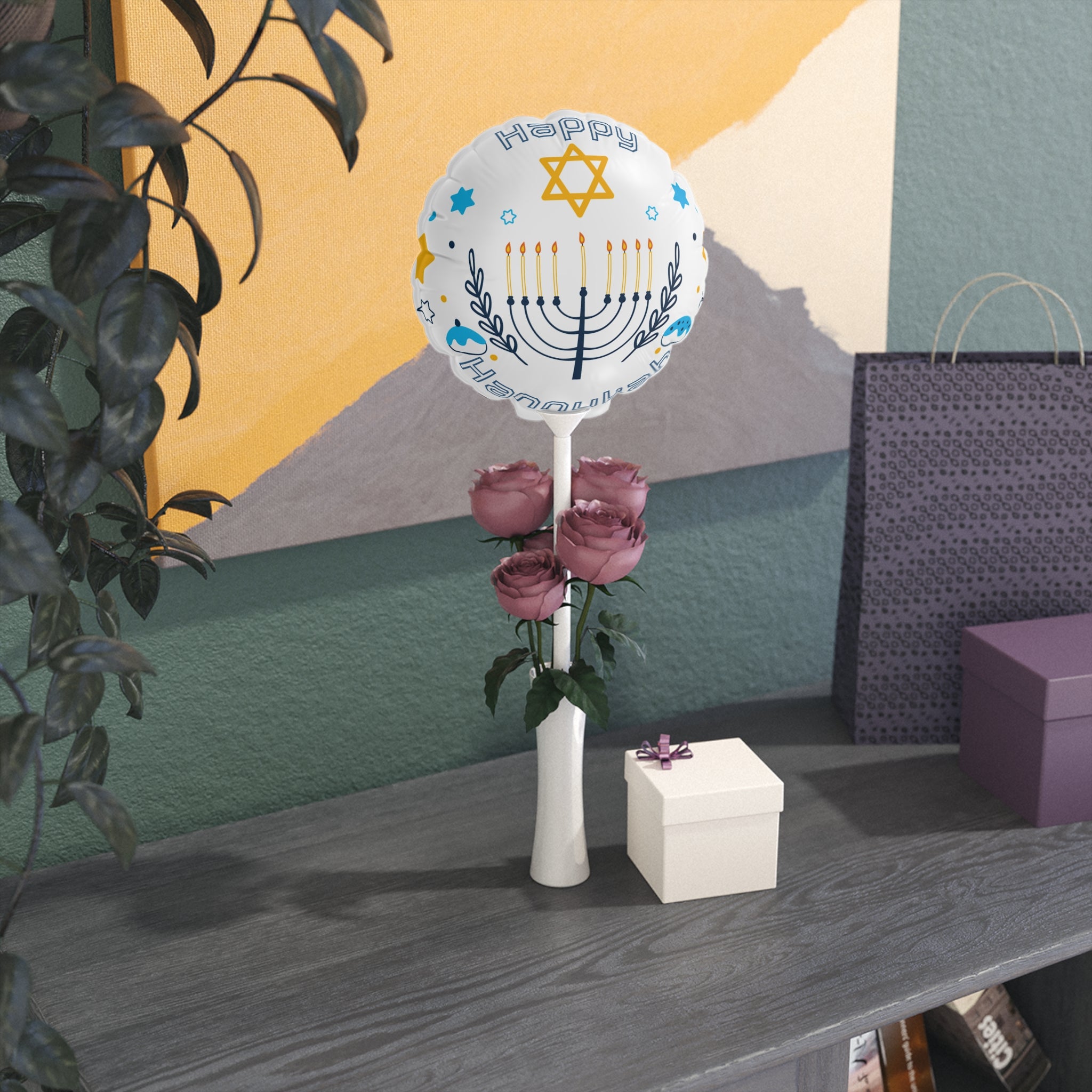 Decorative balloon with Menorah design on a table with flowers and a box against a colorful wall.