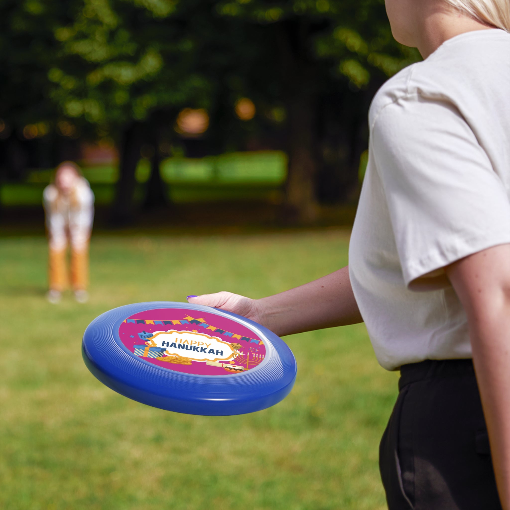 Person holding a colorful frisbee with 'Happy Hanukkah' text in a park setting.