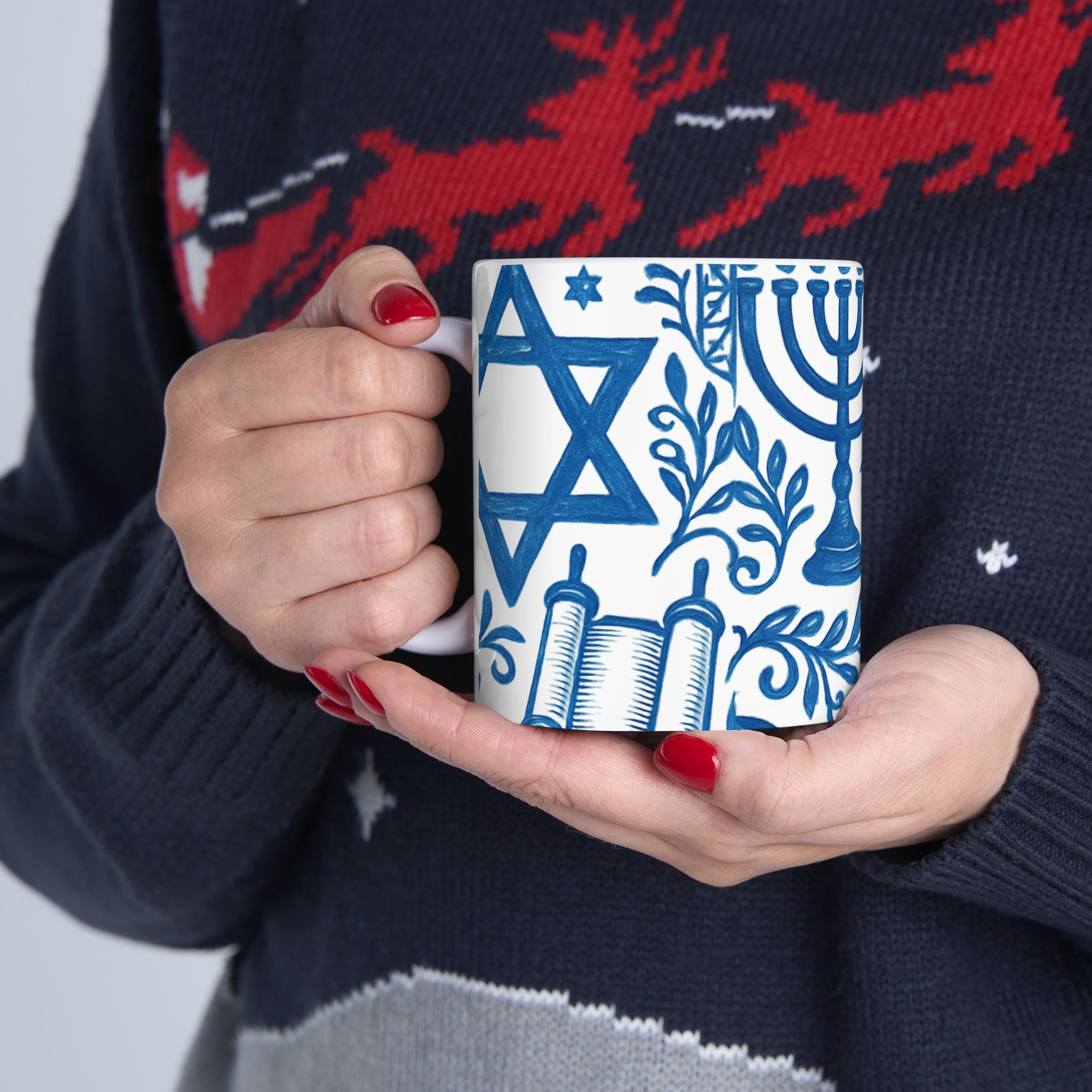 Person holding a mug with Jewish symbols against a dark sweater with red deer design.